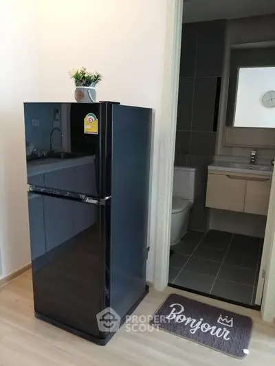 Modern apartment interior with sleek black fridge and stylish bathroom view.