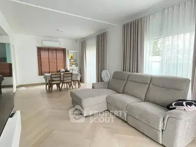 Spacious living room with modern sofa and dining area, featuring large windows and elegant curtains.