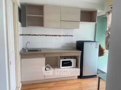 Compact kitchen with modern cabinetry, microwave, and fridge in a cozy apartment setting.