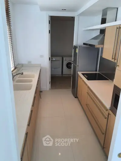 Modern kitchen with sleek cabinetry and stainless steel appliances, featuring a convenient laundry area.
