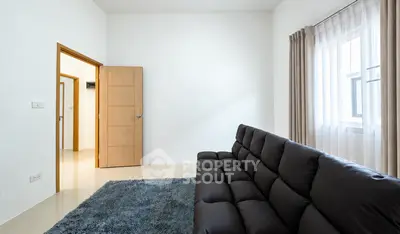 Modern living room with sleek black sofa and plush rug, featuring natural light from large window.