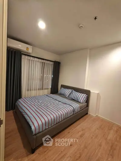 Cozy bedroom with striped bedding and wooden flooring in modern apartment.