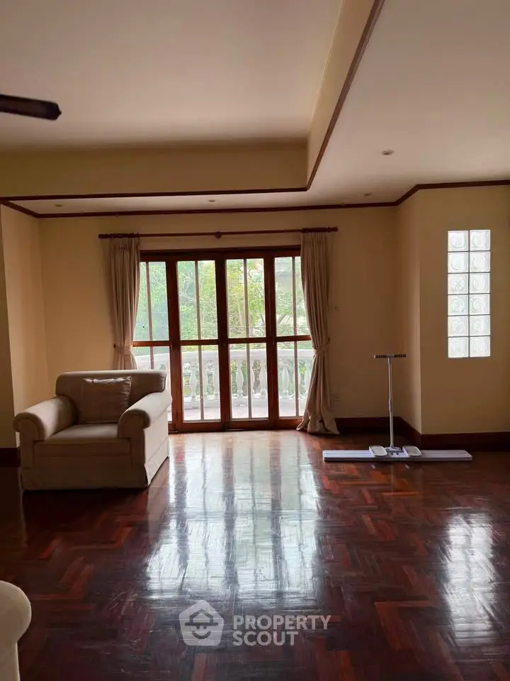 Spacious living room with wooden flooring and large windows opening to a balcony.