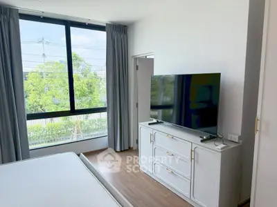 Modern bedroom with large window and flat-screen TV, offering a bright and inviting atmosphere.