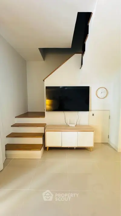 Modern living room with sleek staircase and wall-mounted TV, featuring minimalist design and neutral tones.