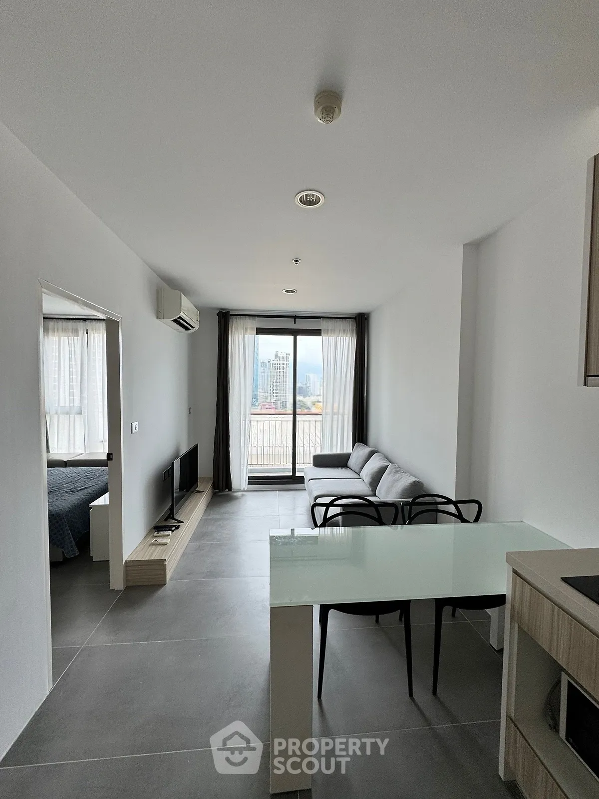 Modern open-plan living room with sleek furniture and city view from balcony.