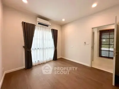 Spacious empty room with wooden flooring and large window, perfect for customization.