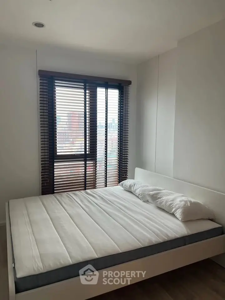 Modern bedroom with large window and city view, featuring a minimalist bed and sleek blinds.