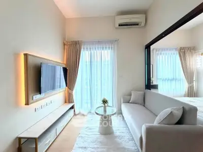 Modern living room with sleek design, featuring a wall-mounted TV, elegant sofa, and large windows with sheer curtains.