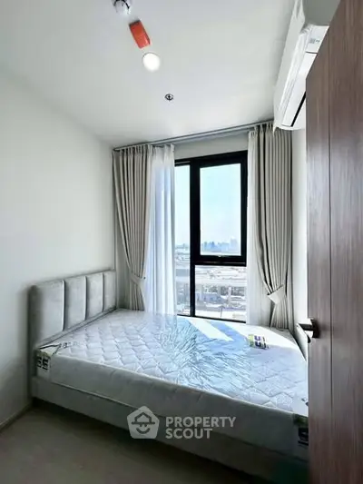 Bright bedroom with large window and modern furnishings in a high-rise apartment.