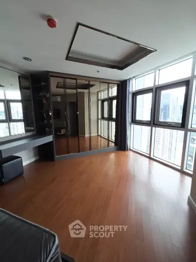 Spacious modern living room with wooden flooring and large windows offering city views.