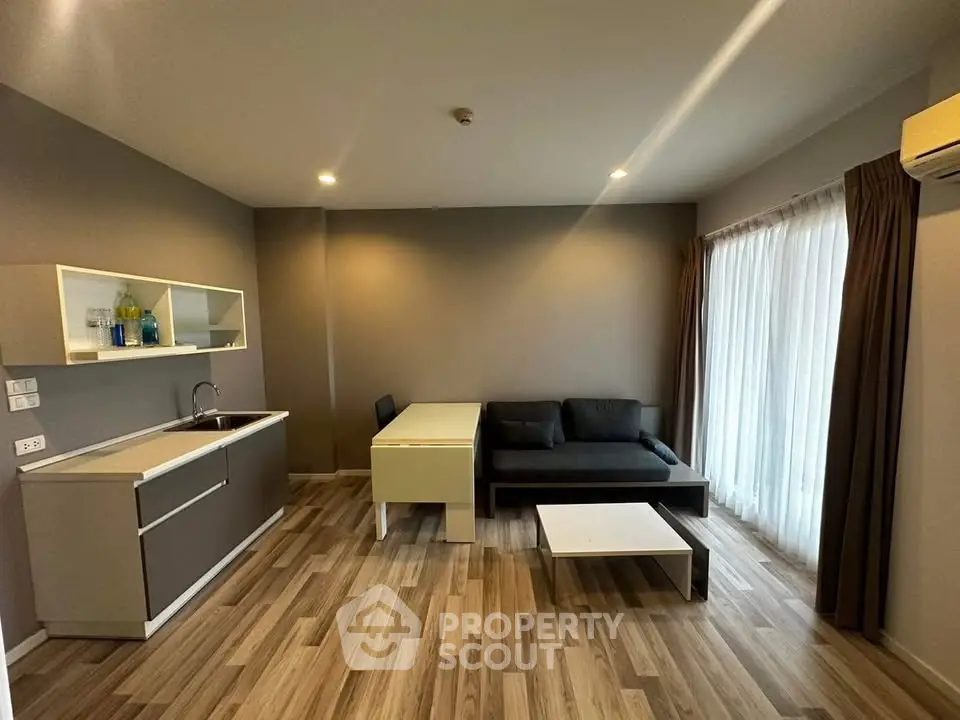 Modern living room with sleek furniture and open kitchen layout, featuring natural light and stylish decor.