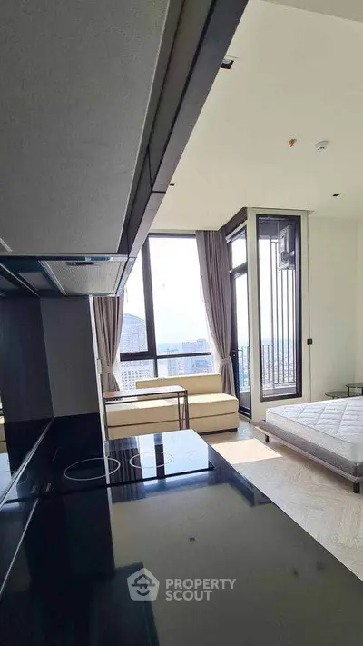 Modern studio apartment with sleek kitchen and large windows offering city views.