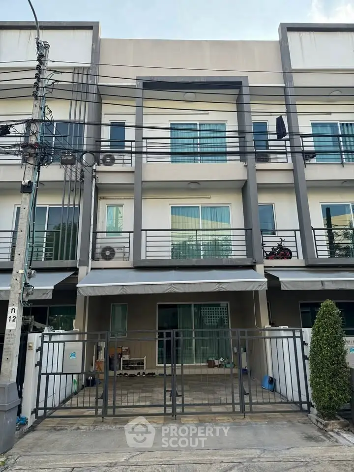 Modern three-story townhouse with gated entrance and balconies in urban setting.