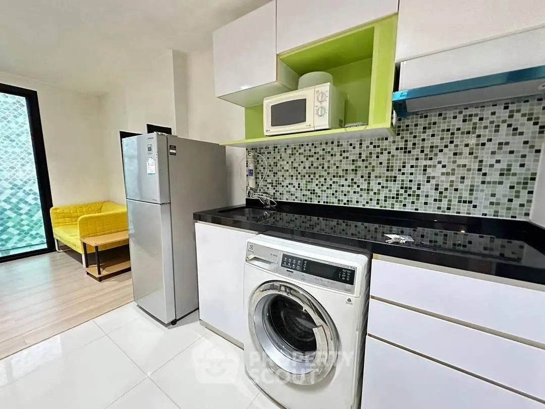 Modern kitchen with washing machine, fridge, and microwave in stylish apartment.