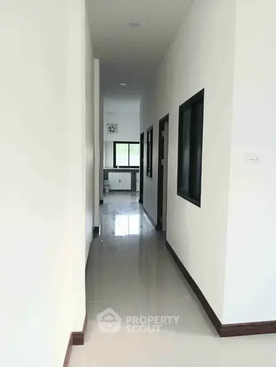 Bright hallway leading to a modern kitchen with sleek finishes and large windows.
