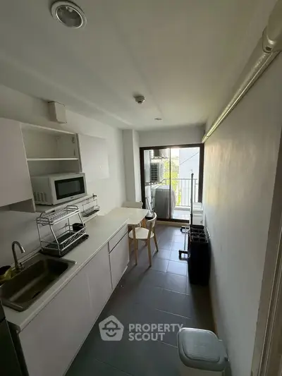 Modern compact kitchen with sleek design and balcony access, featuring a microwave and ample storage.