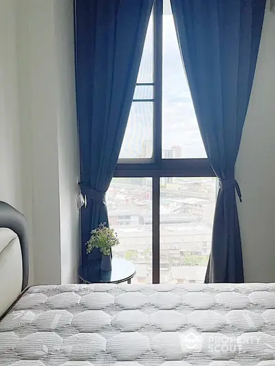 Cozy bedroom with a large window offering an expansive city view, adorned with elegant navy blue curtains, creating a serene urban retreat.