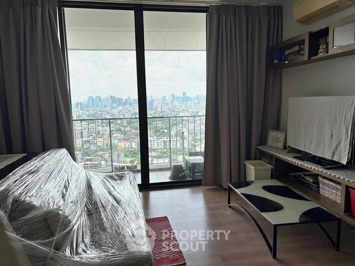 Modern living room with city view and balcony, featuring a wrapped sofa and stylish decor.