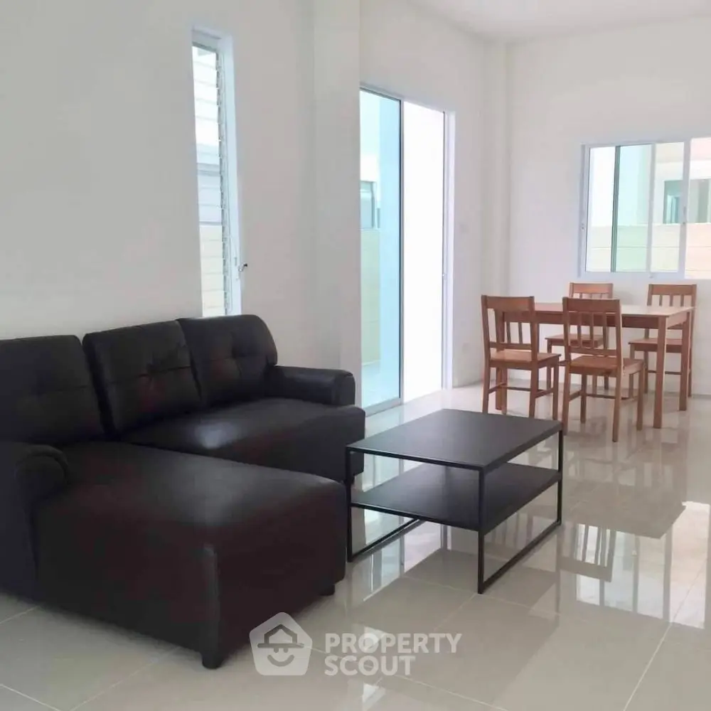 Modern living room with sleek black sofa and dining set in bright open space.
