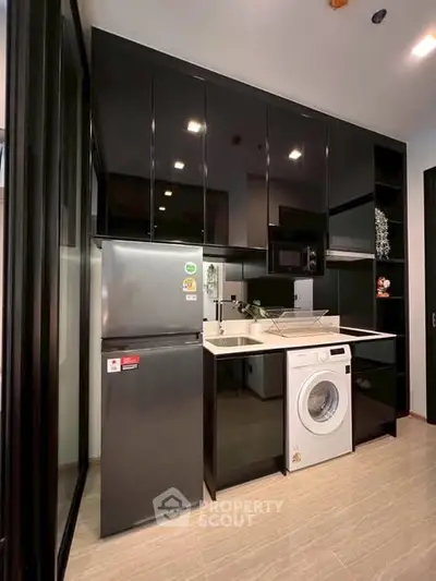 Modern kitchen with sleek black cabinets, fridge, and washing machine in a compact layout.