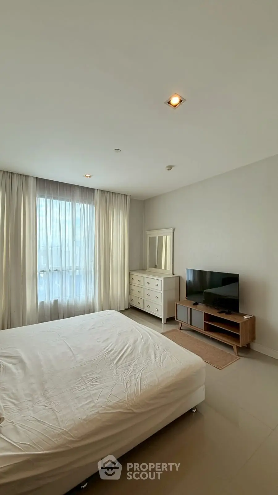 Spacious bedroom with natural light, modern furnishings, and a sleek TV setup.