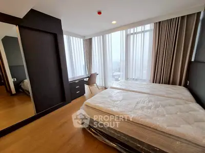 Spacious bedroom with large windows and modern furnishings in a high-rise apartment.