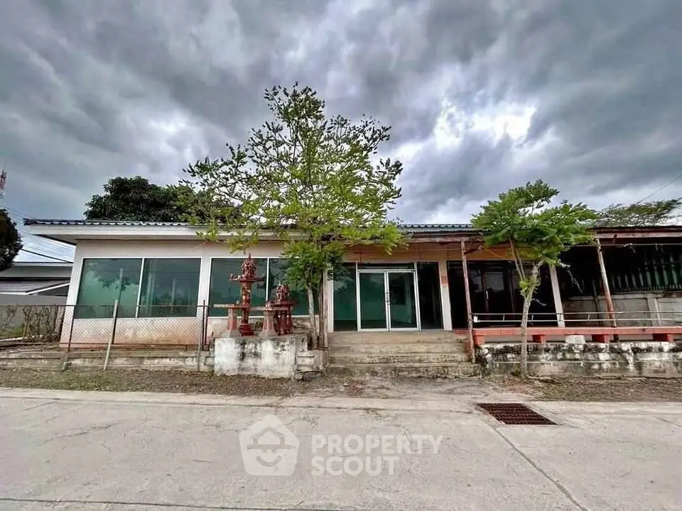 Charming single-story home with large windows and lush greenery under a dramatic sky.