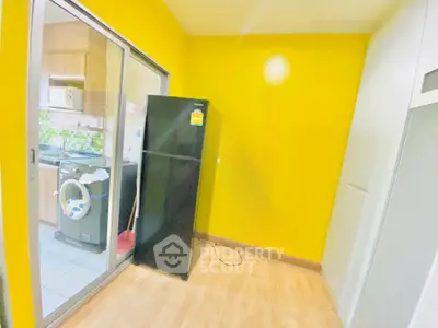 Bright kitchen with yellow walls, featuring a black fridge and washing machine, ideal for modern living.