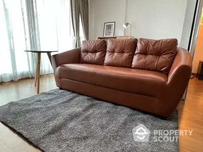 Elegant living space featuring a luxurious brown leather sofa on a plush gray rug, complemented by sheer curtains and natural light.