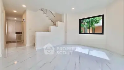 Spacious modern living room with large window and elegant staircase, featuring sleek white flooring.
