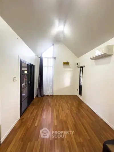 Spacious living room with high ceiling and wooden flooring, featuring modern air conditioning.
