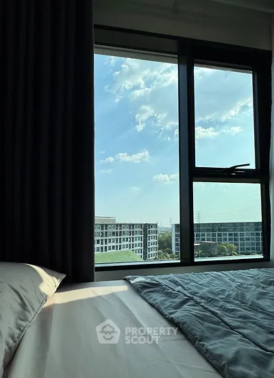 Cozy bedroom with large window offering stunning city view and natural light.