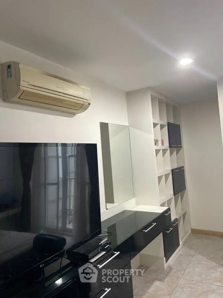 Modern living room with sleek black furniture and built-in shelving, featuring a wall-mounted air conditioner.
