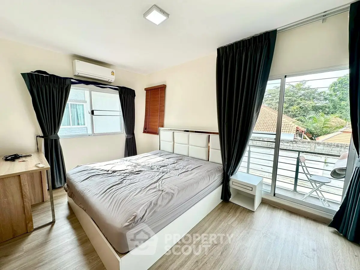 Bright bedroom with large windows and balcony access, featuring modern furnishings and natural light.