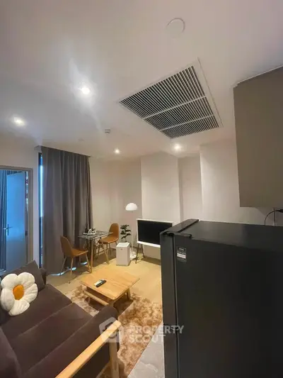 Modern living room with cozy seating and stylish decor, featuring a sleek black refrigerator and ambient lighting.