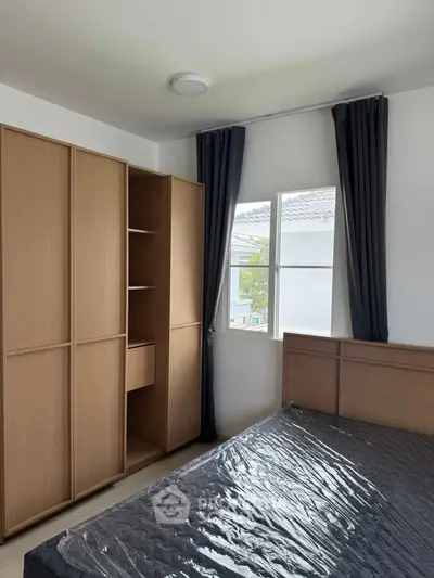 Modern bedroom with sleek wooden wardrobe and large window offering natural light.