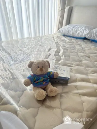 Cozy bedroom with plush teddy bear on a neatly made bed, inviting natural light through sheer curtains.