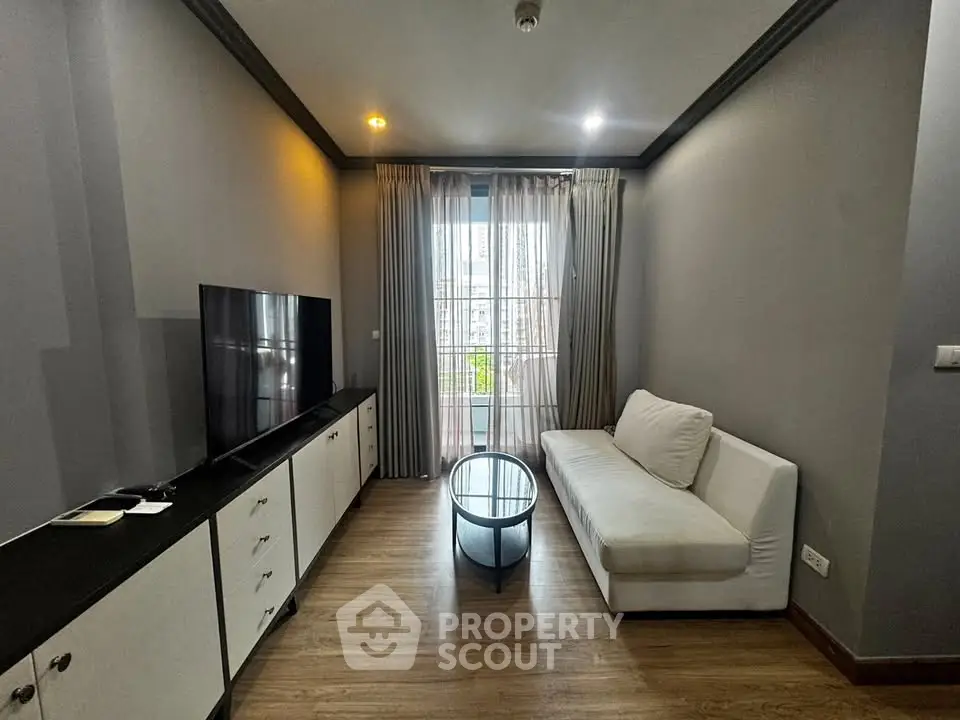 Modern living room with sleek furniture and large window offering city views.