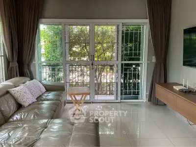 Spacious living room with leather sofa and large windows overlooking lush greenery.