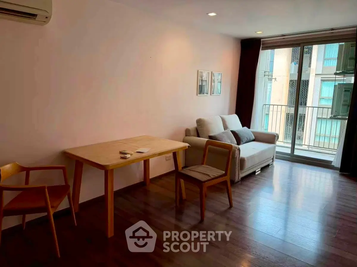 Cozy living room with wooden flooring, modern furniture, and balcony access in a stylish apartment.