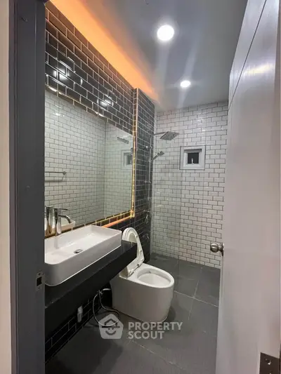 Modern bathroom with sleek black tiles and illuminated mirror