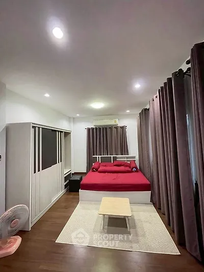 Spacious bedroom with red bedding and modern decor, featuring ample natural light and sleek furnishings.