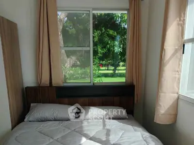 Cozy bedroom with large window offering lush green garden view, perfect for relaxation.