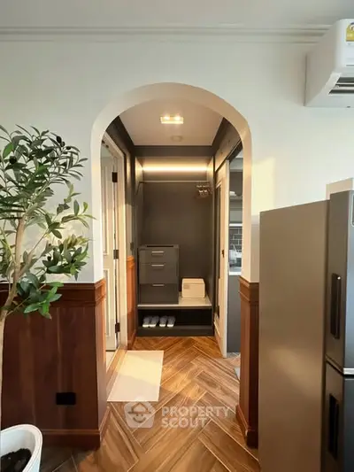 Stylish interior with modern wood flooring and archway leading to a storage area, featuring sleek appliances.