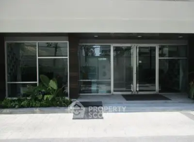 Modern building entrance with glass doors and lush greenery