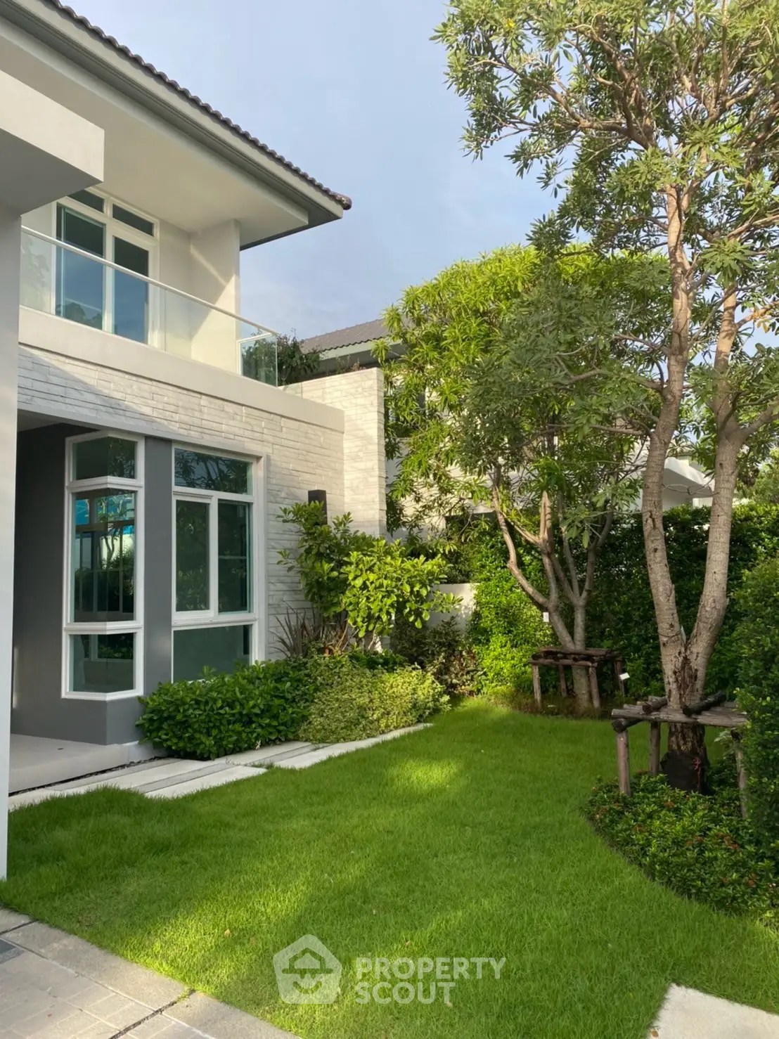 Charming modern house exterior with lush green garden and large windows, perfect for serene living.