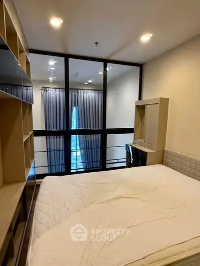 Modern bedroom with large window and built-in shelving, offering a cozy and functional living space.