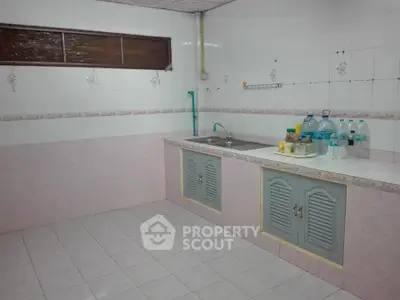 Spacious kitchen with tiled walls and floor, featuring a sink and ample counter space.