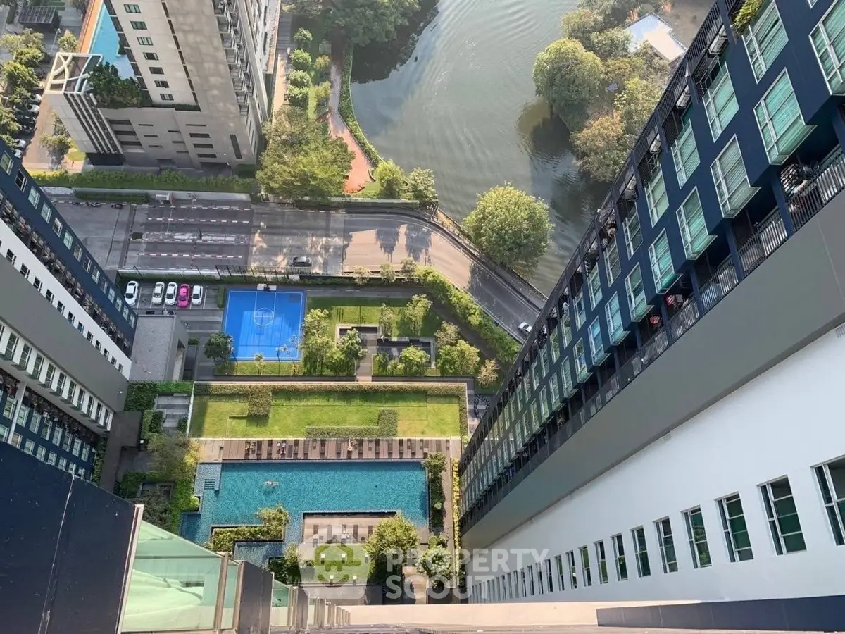 Stunning aerial view of modern high-rise building with pool and sports court, overlooking lush greenery and serene water.